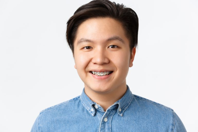 Orthodontics, dental care and stomatology concept. Close-up portrait of handsome asian man with teeth braces, smiling pleased, looking hopeful and happy, standing white background
